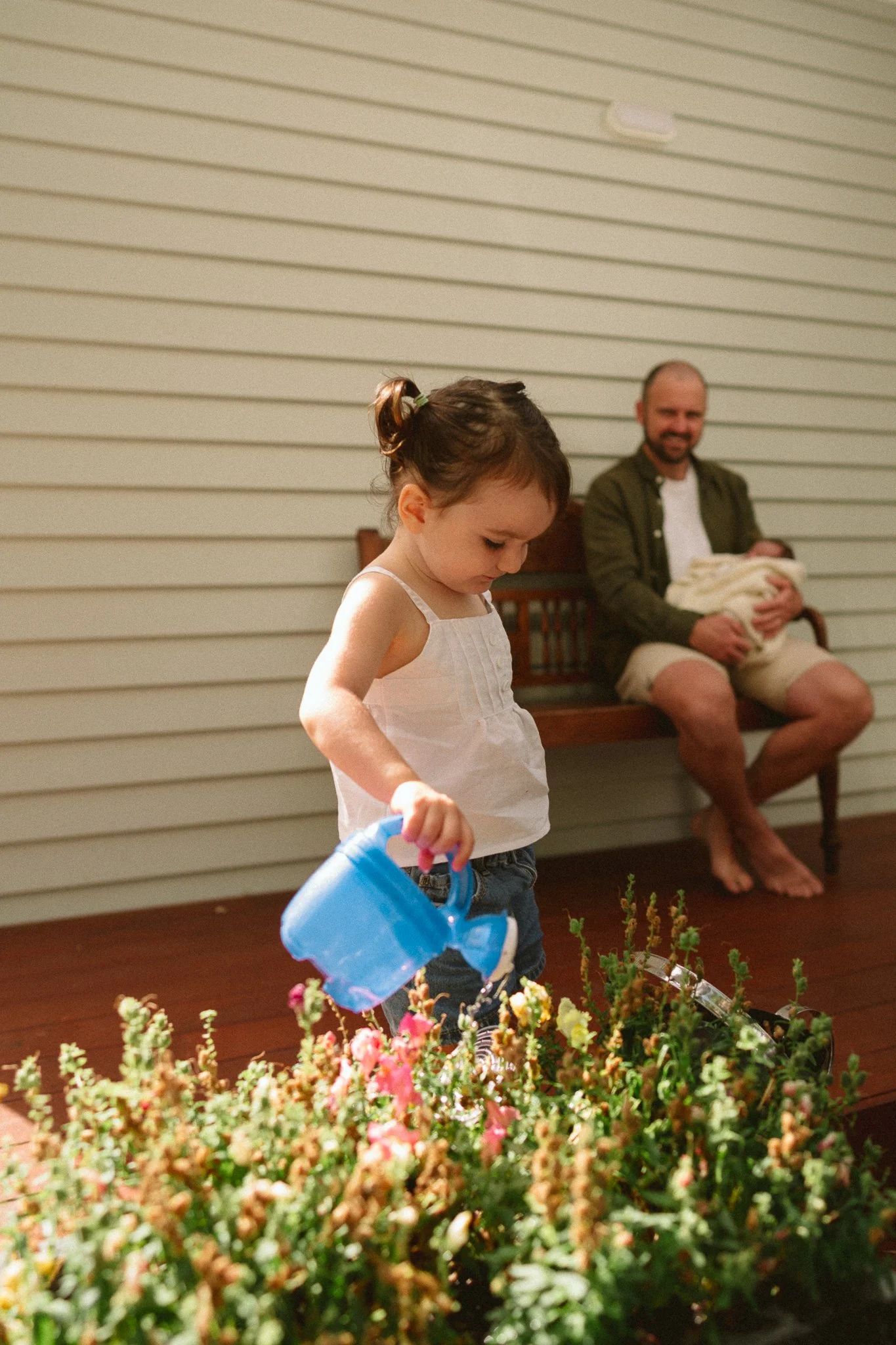 A little girl watering her flowers, while Dad watches on with joy during a newborn photoshoot in Christcurch, NZ.