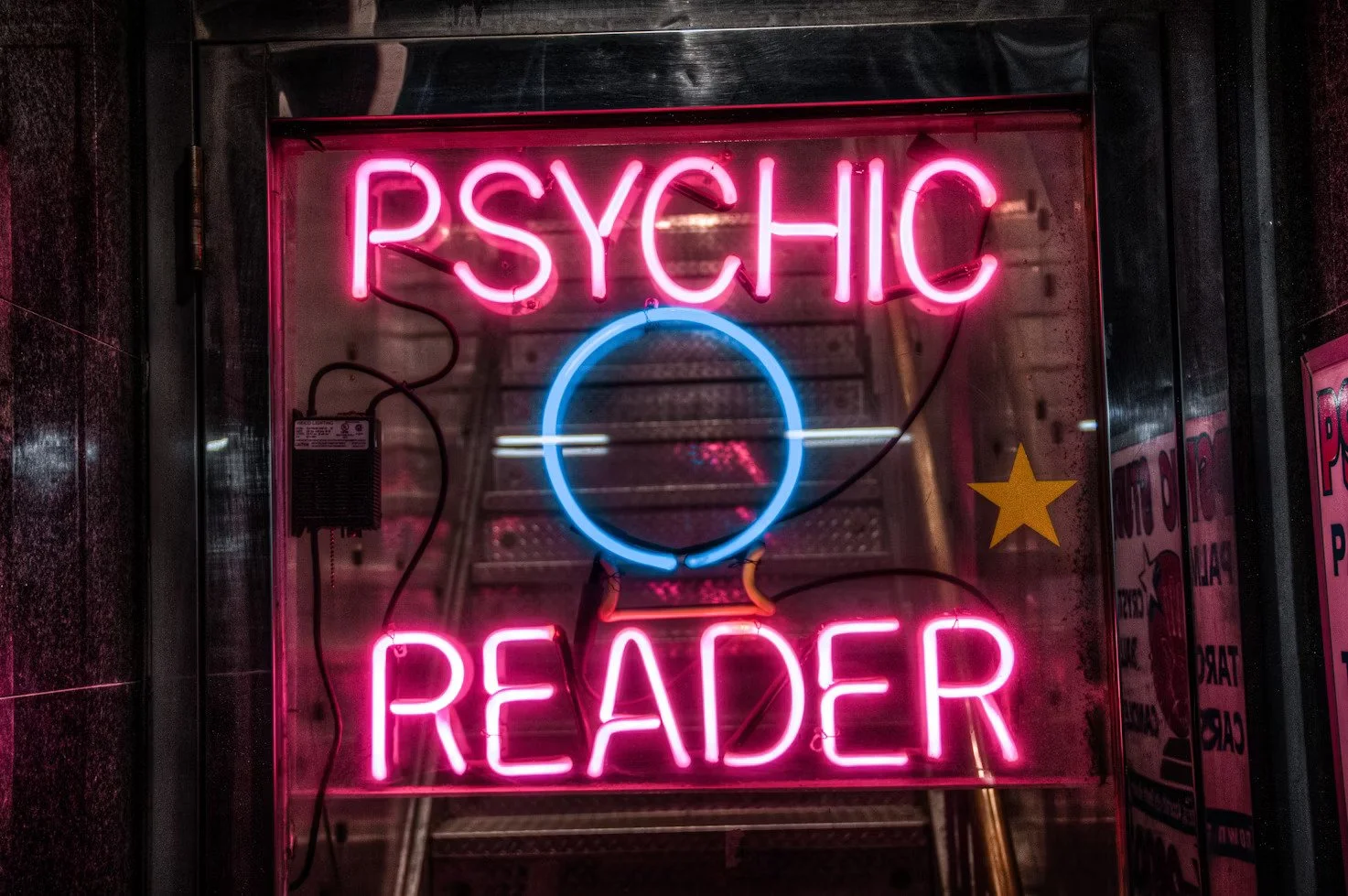 Neon sign reading 'Psychic Reader' in pink with a blue circle in the center.