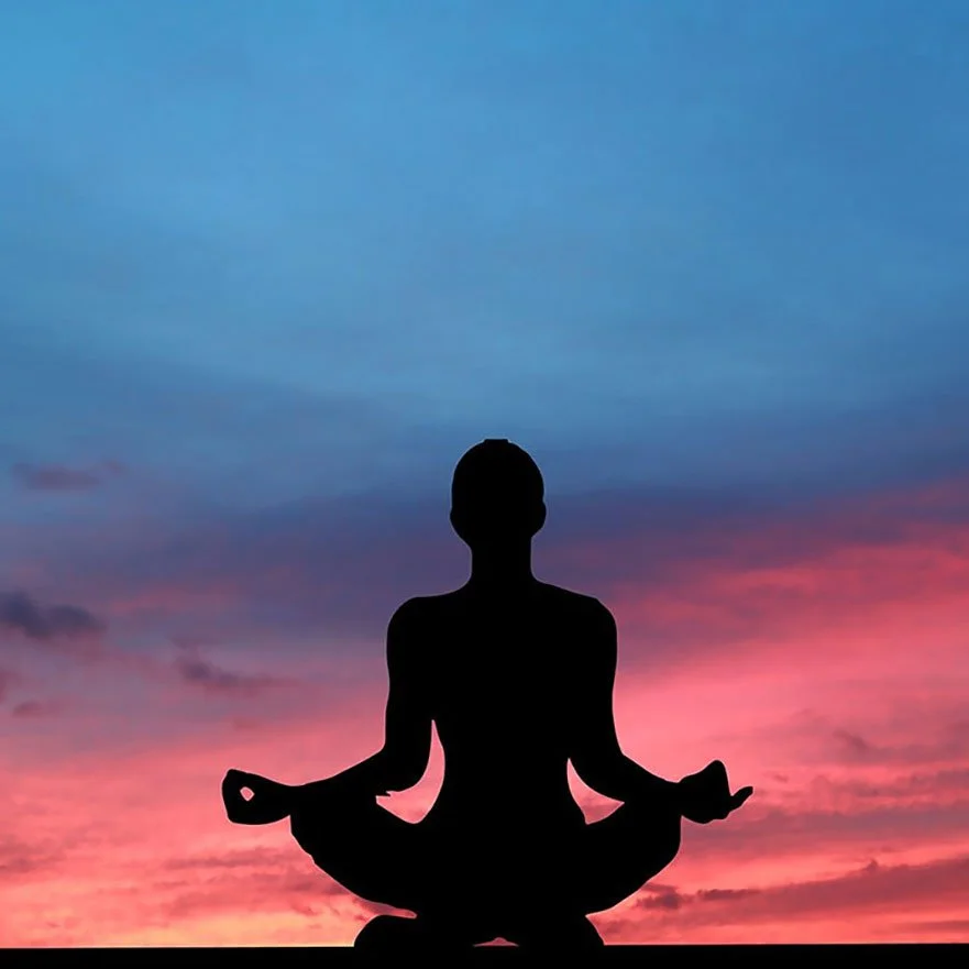Silhouette of a person meditating outdoors against a colorful sunset sky with shades of pink, purple, and blue.