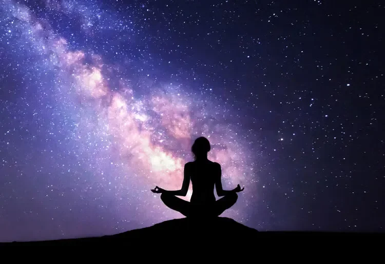 Silhouette of a person sitting cross-legged in meditation on a hilltop under a starry night sky with the Milky Way galaxy visible.