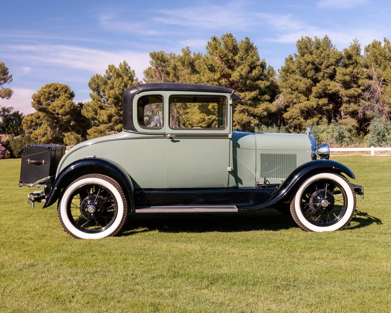 A vintage green and black 1928 Ford Model A Special Coupe parked on grass with trees and blue sky in the background. Classic car experiences by Gabby Lane Classics.