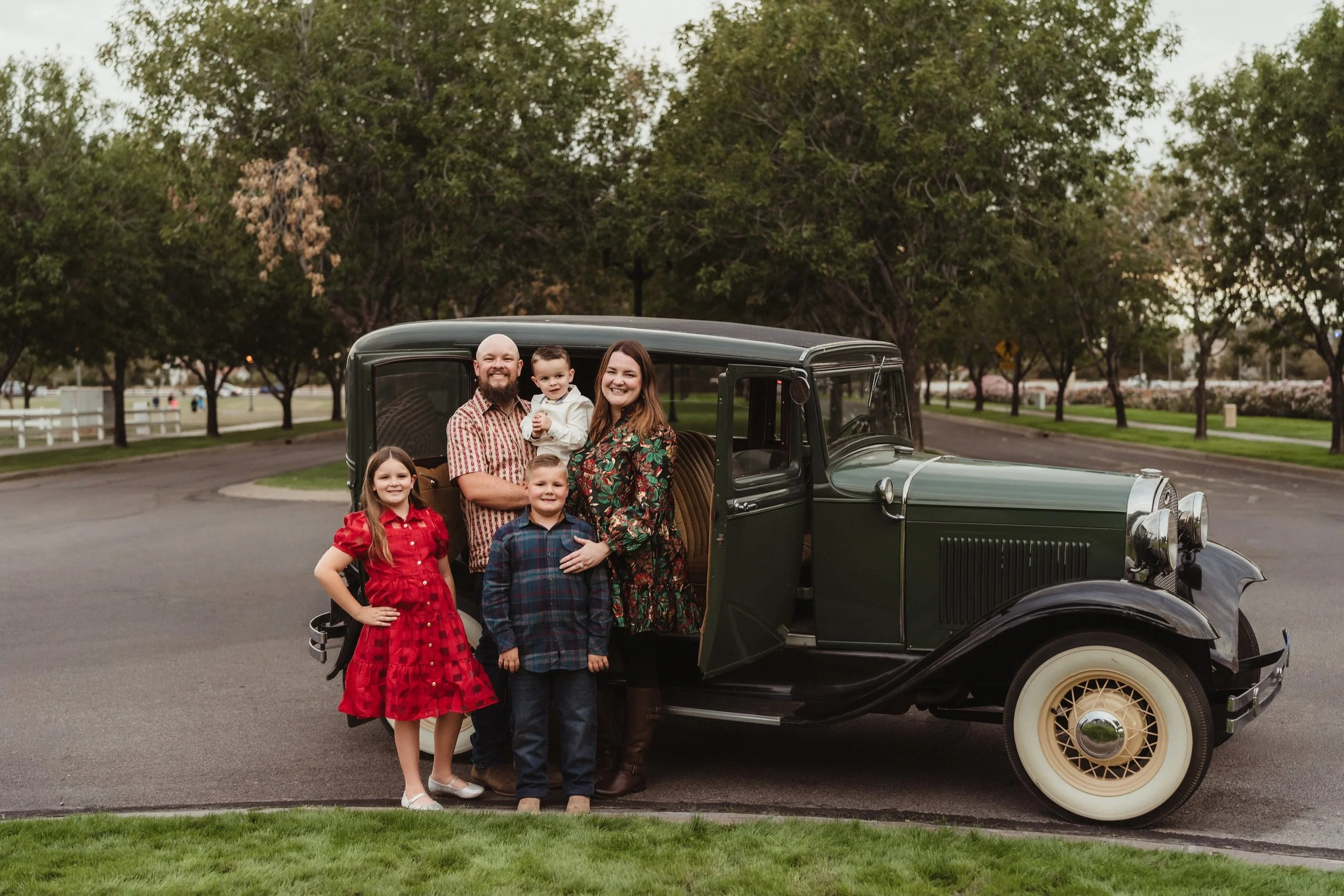 Owners of Gabby Lane Classics, Marie and Shane, family photo of five posing outdoors next to a vintage 1931 Ford Four Door ("Green") car. 