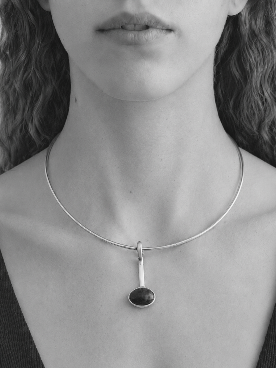 Close-up of a woman wearing a silver necklace with a black oval pendant.