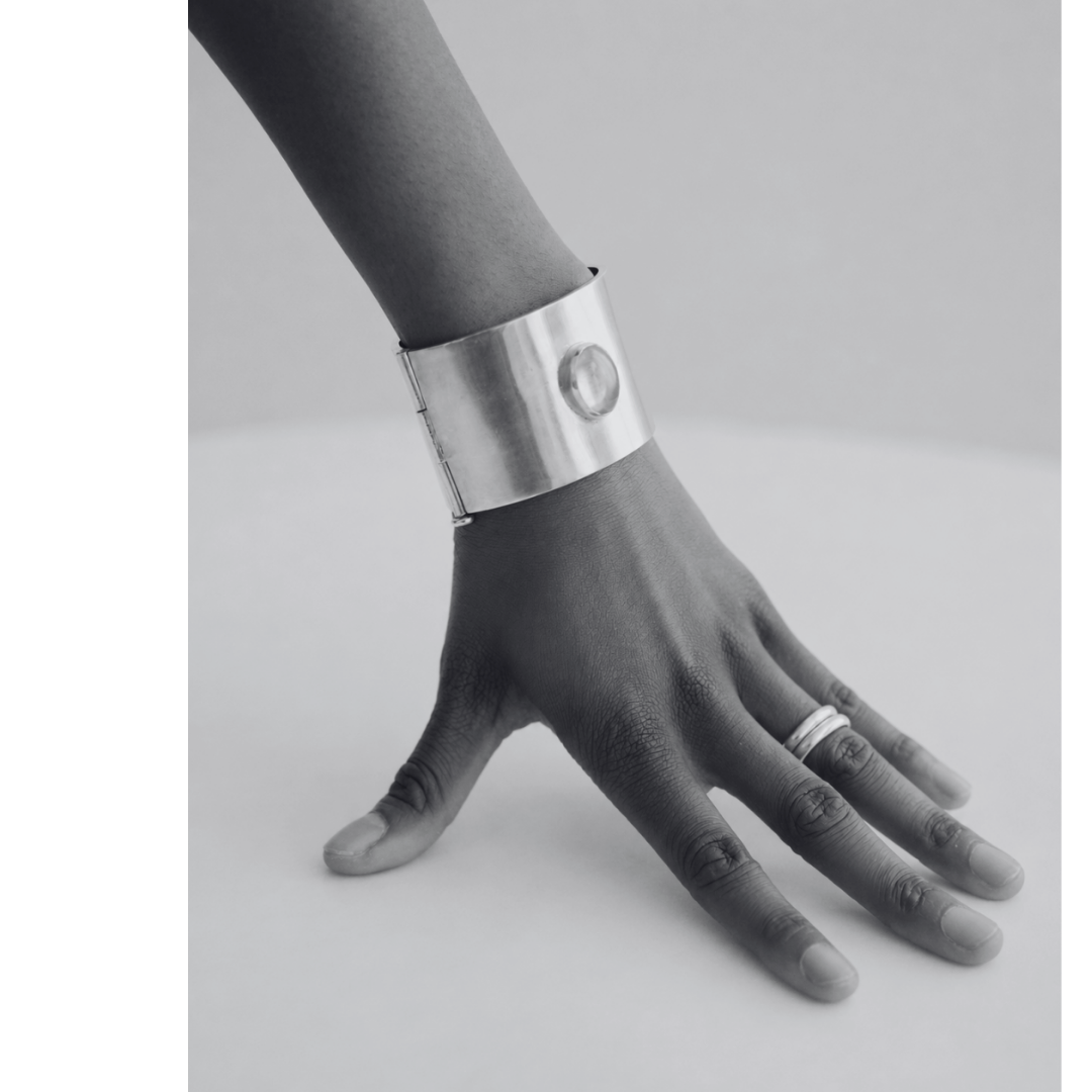 A black and white photo of a hand with fingers extended onto a flat surface, wearing a large metallic cuff bracelet and a ring on the ring finger.