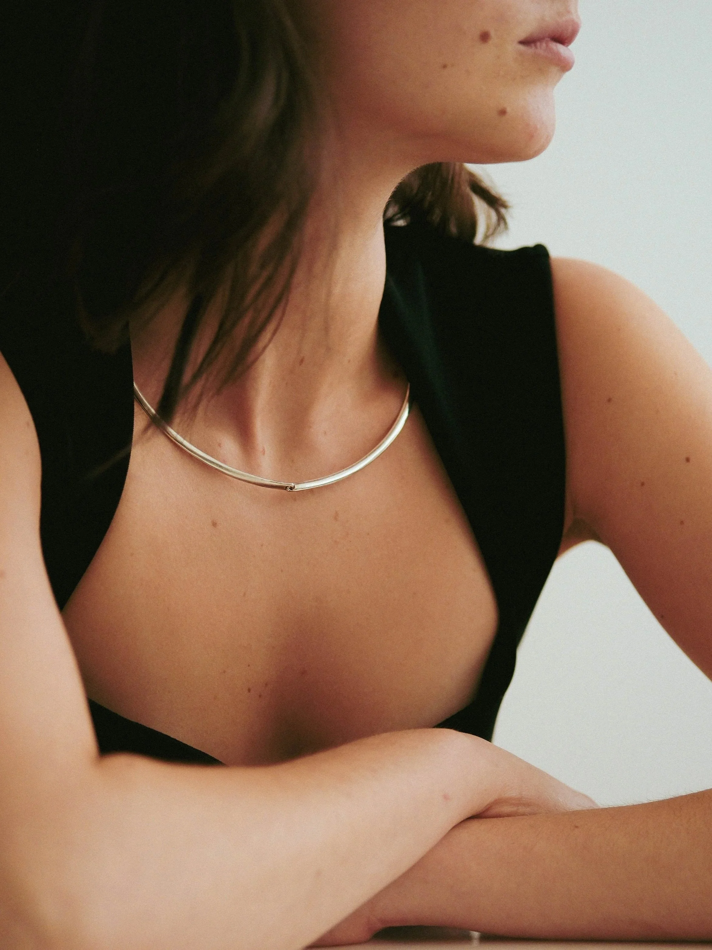 Close-up of a woman's face, showing her lips, chin, and a small mole on her cheek, with dark hair framing her face, wearing a black top and a silver necklace.