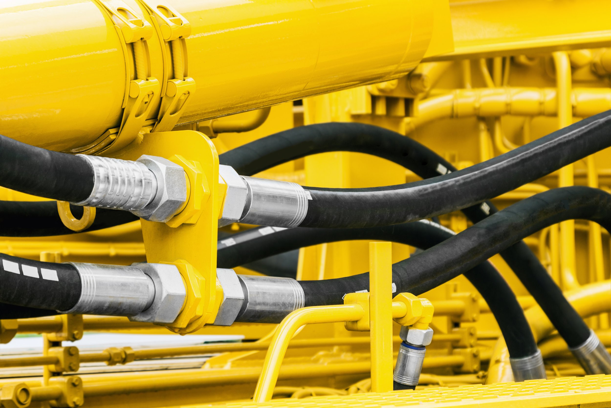 Close-up of yellow industrial piping system with black hoses connected using metal fittings and yellow brackets.