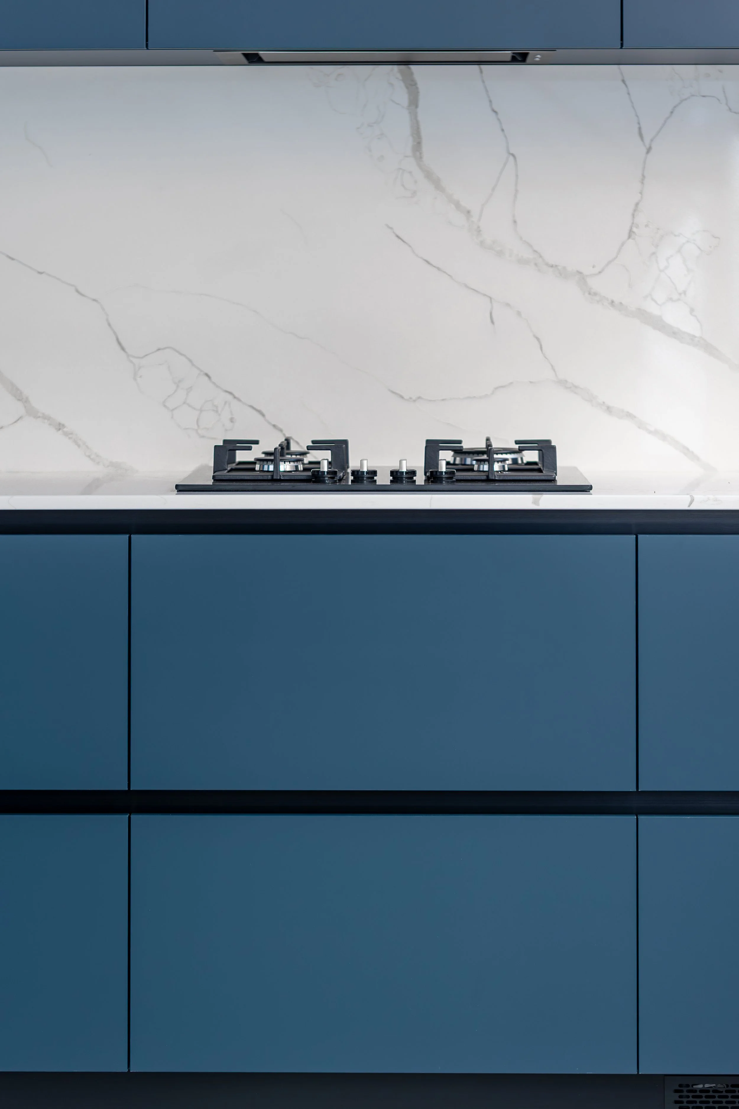 Moderne keuken met blauwe kasten en inductiekookplaat, witte marmeren achterwand.