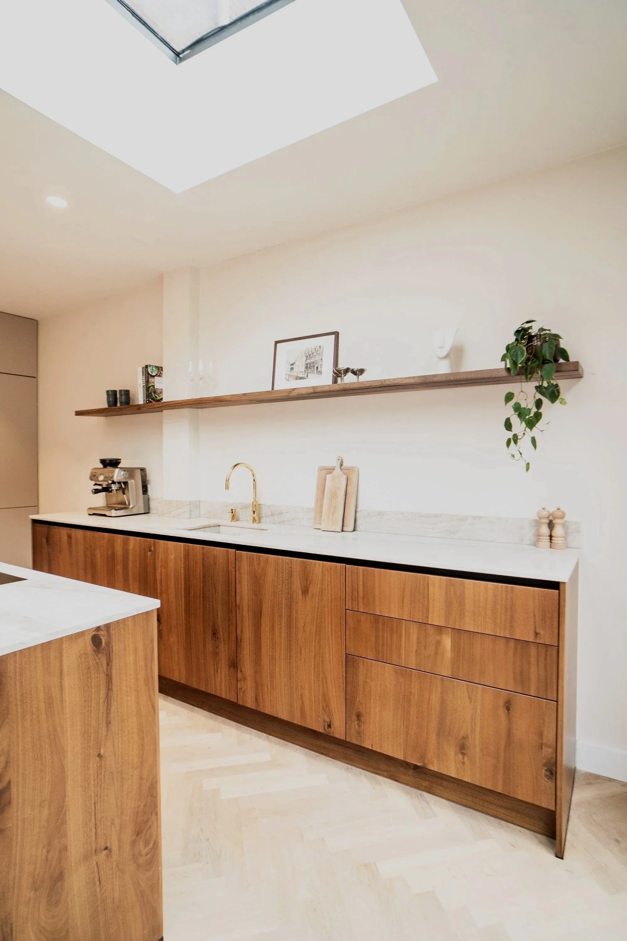 Een moderne keuken met witte muren en houten kasten, een houten plank boven de gootsteen, decoratieve accessoires en een plant.