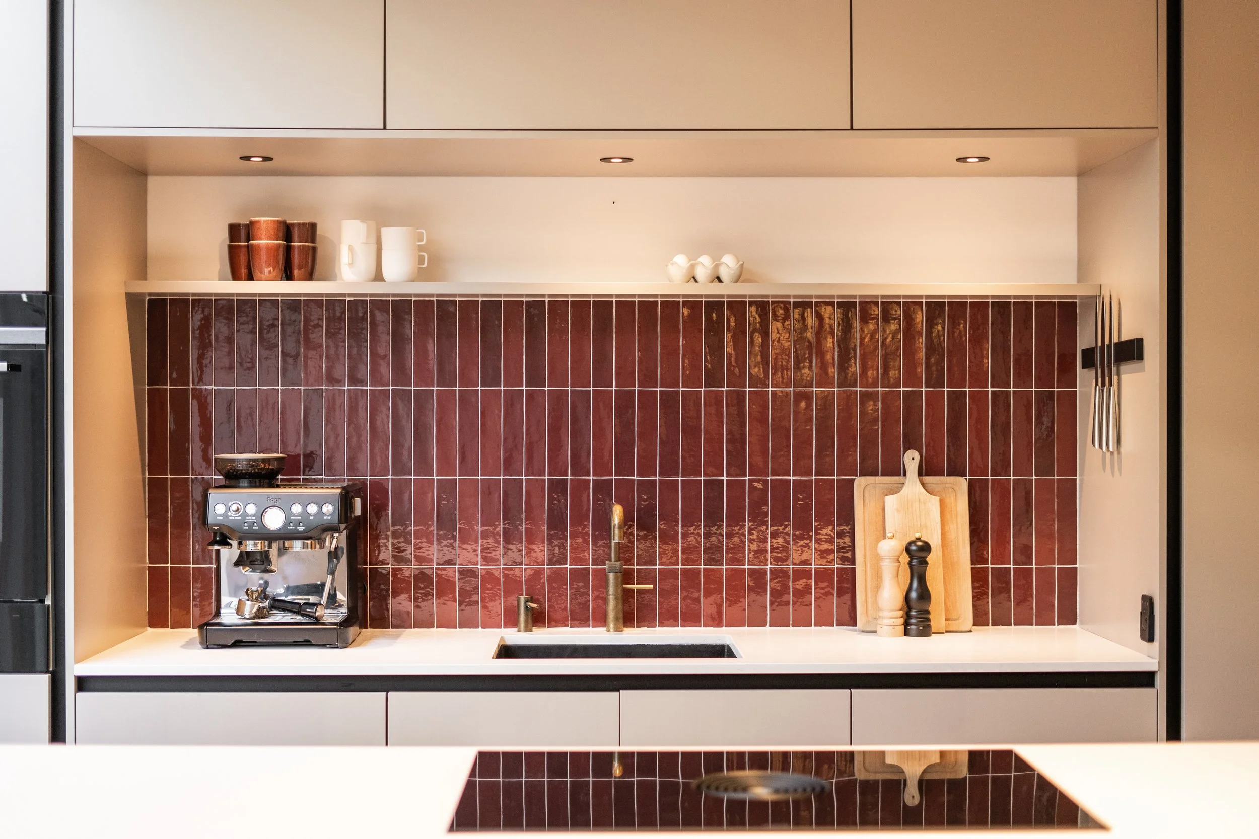 Moderne keuken met zwarte en witte kasten, een koffiezetapparaat, snijplanken, en keukengerei in minimalistische stijl.