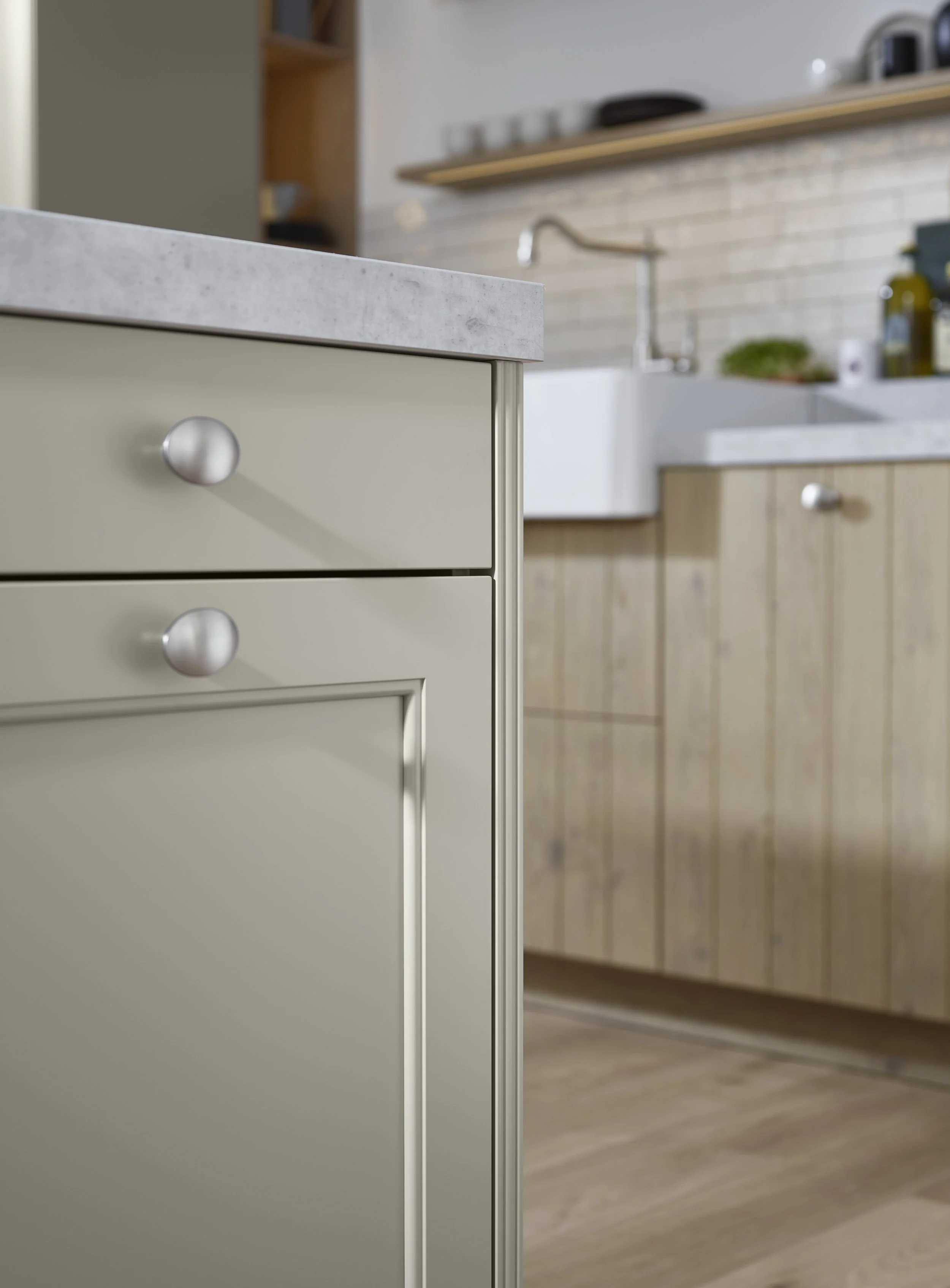 Close-up van een keukenblok met grijze laden en een marmeren werkblad, met een dubbele keukenbak en houten kasten op de achtergrond.