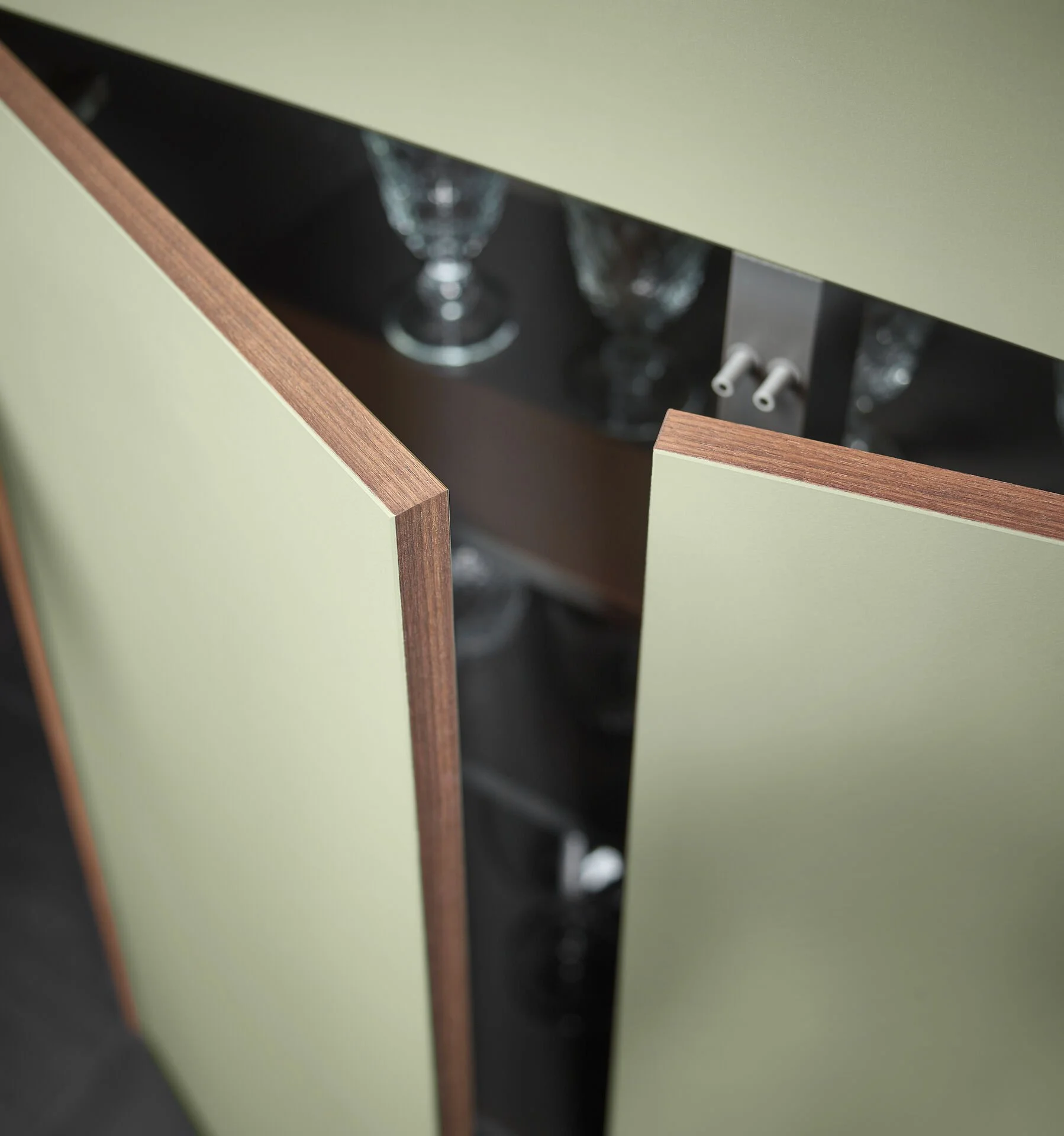 Een groene kast met houten randen, waarvan de deuren iets openstaan, waarin glazen zijn te zien.