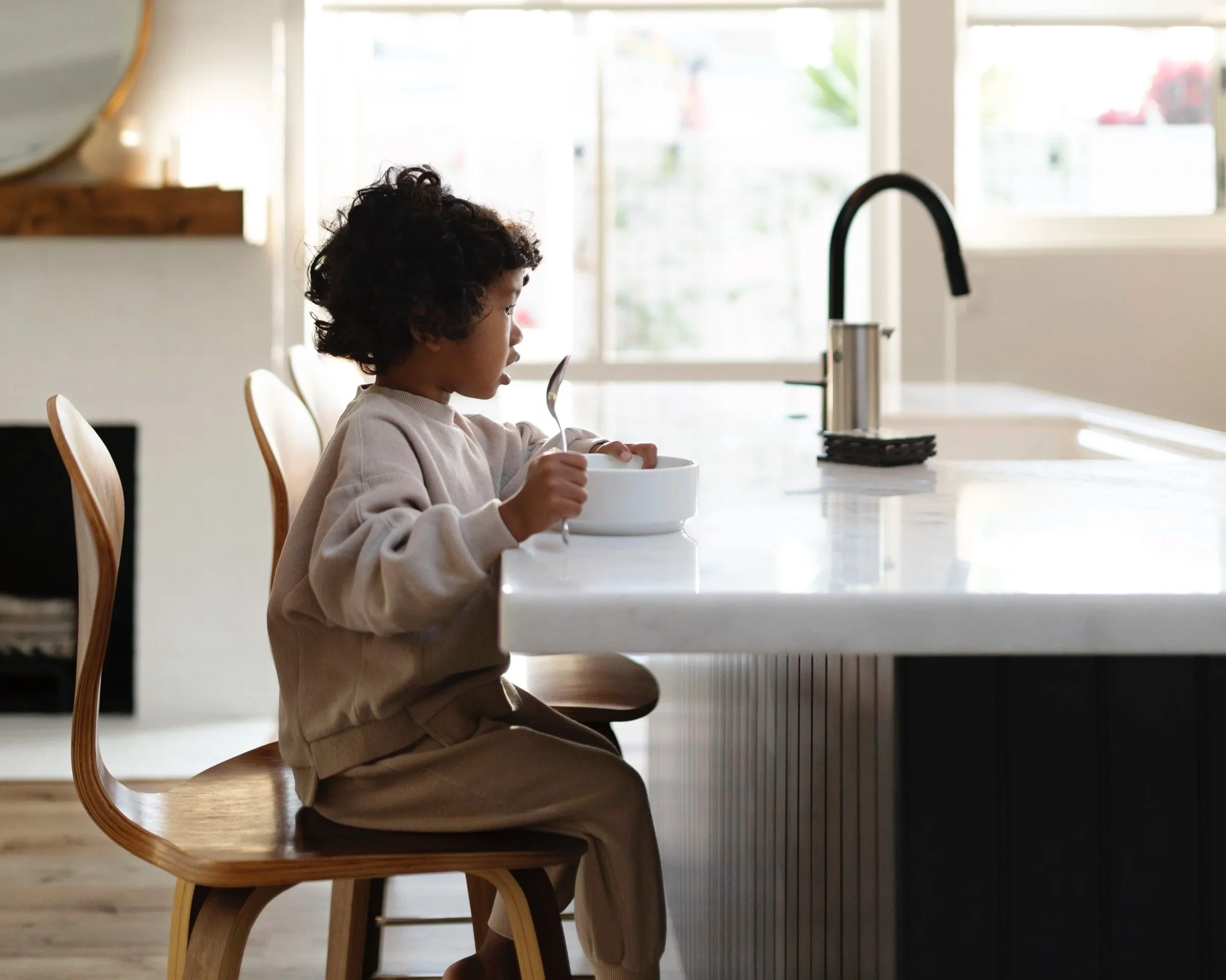 Kind eet soep aan een witte keuken eettafel met een lepel in de hand.