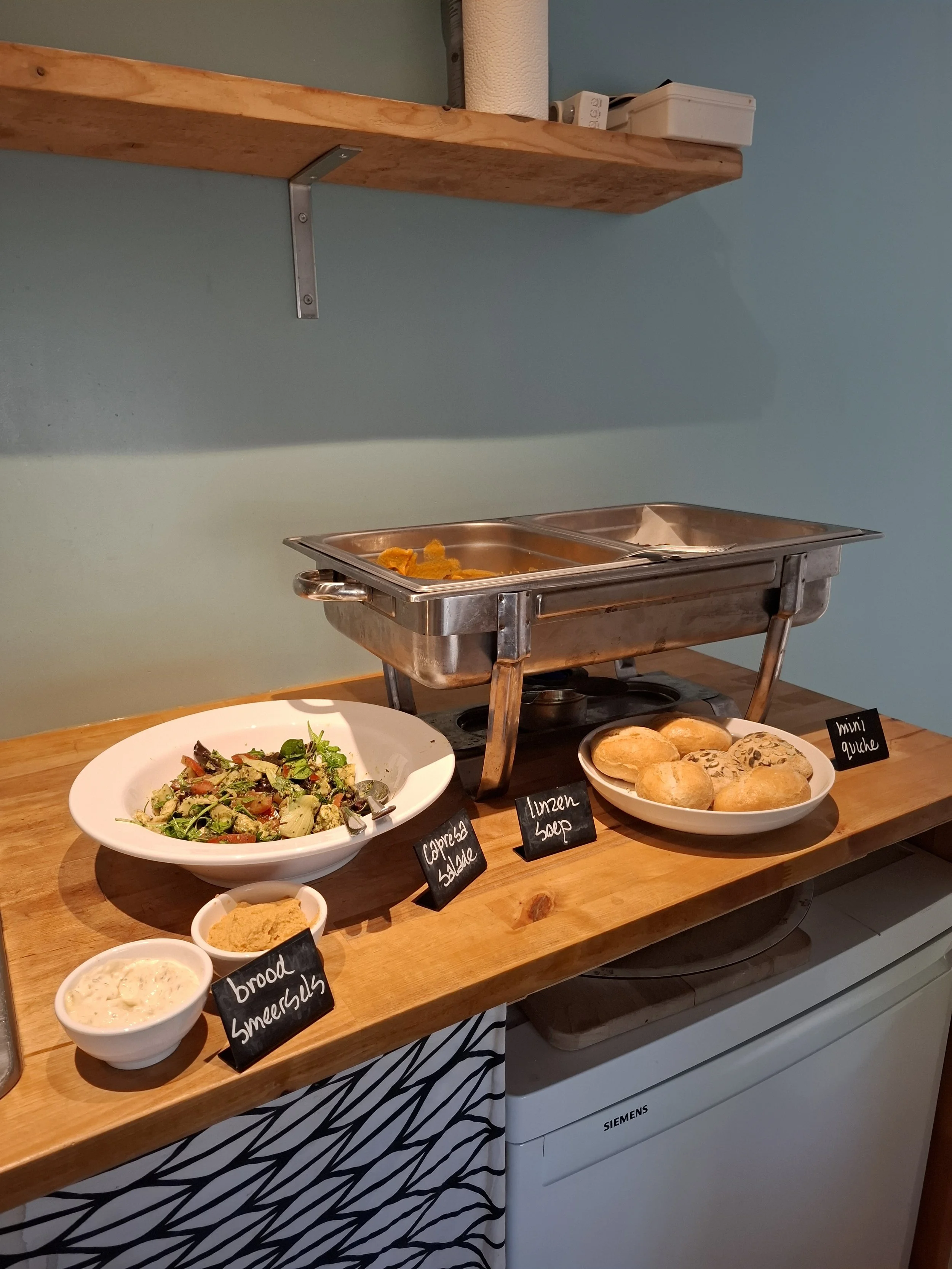 Een buffet met salade, brood, smeersels, en mini quiches. 