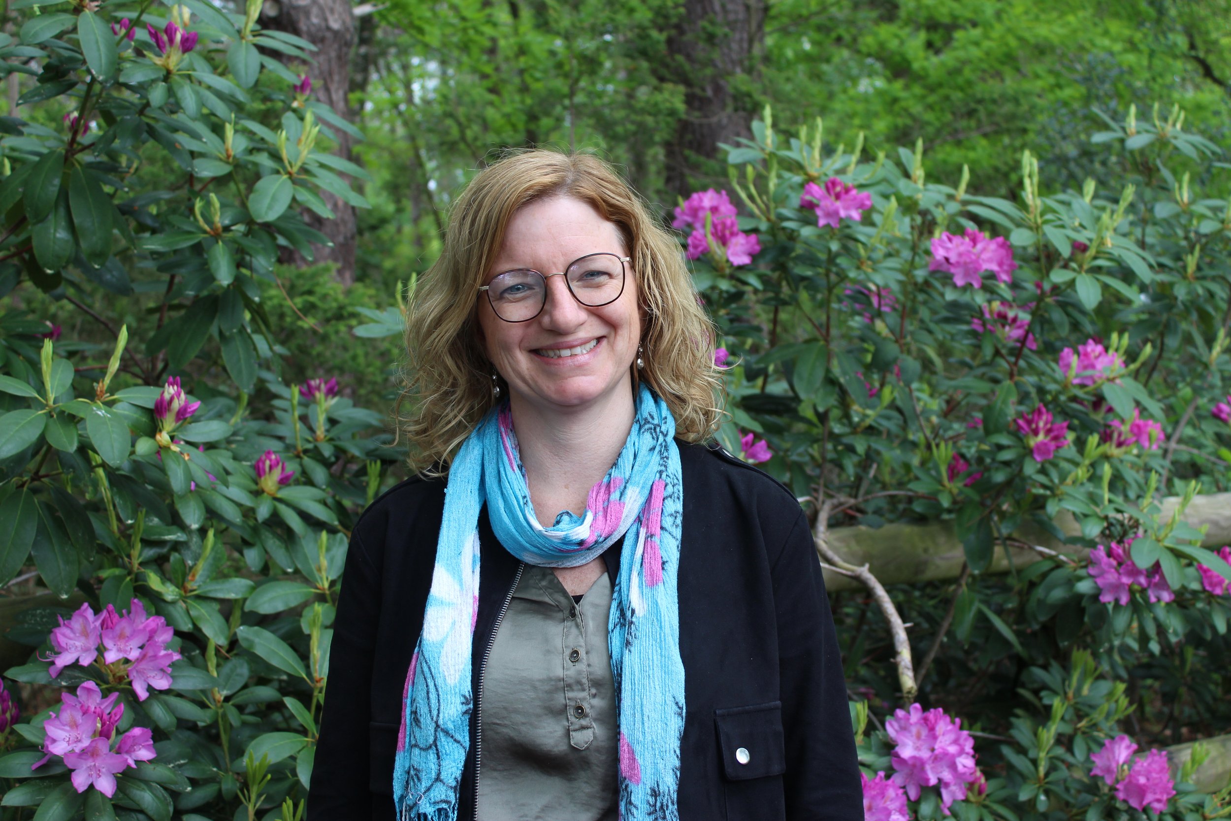 Marieke Buijsse-van der Heijden, natuurcoach, straalt te midden van roze bloemen in de natuur.
