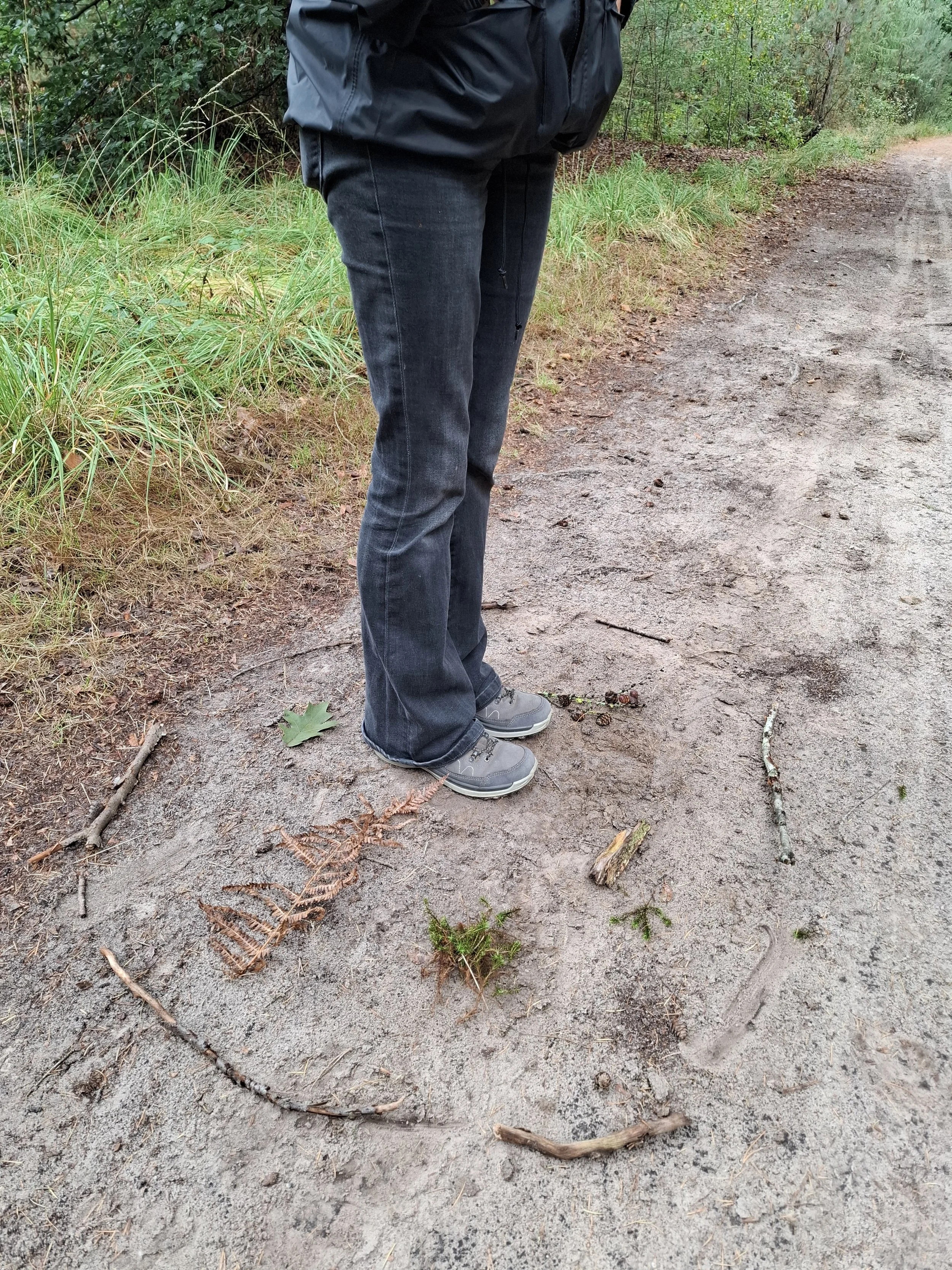 Deelneemster staat op een bospad, omringd door natuurlijke elementen zoals takken en bladeren, in haar zelfgemaakt kwaliteitencirkel.