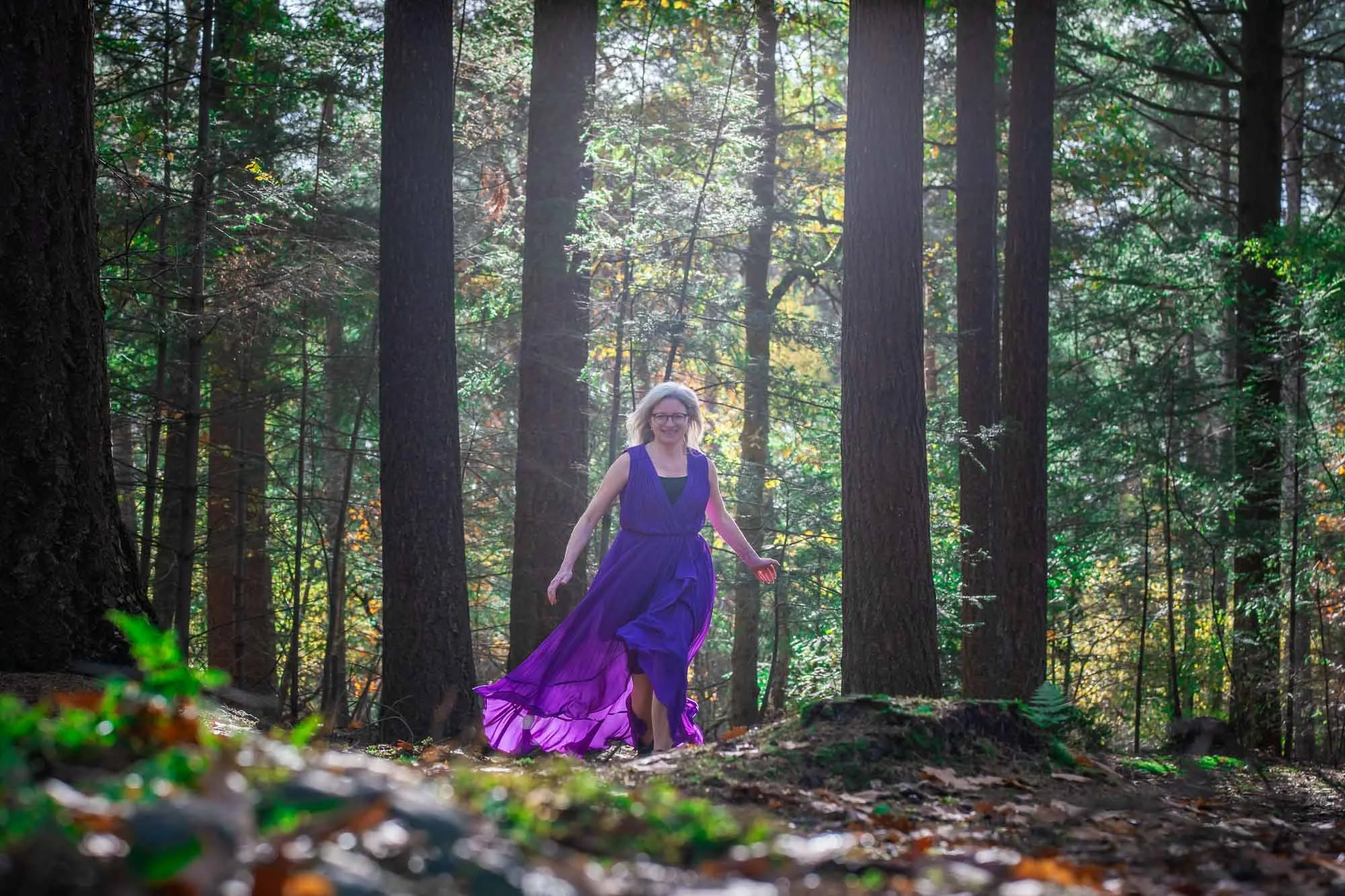 Marieke natuurcoach rent blij en vrij door het bos in een paarse jurk