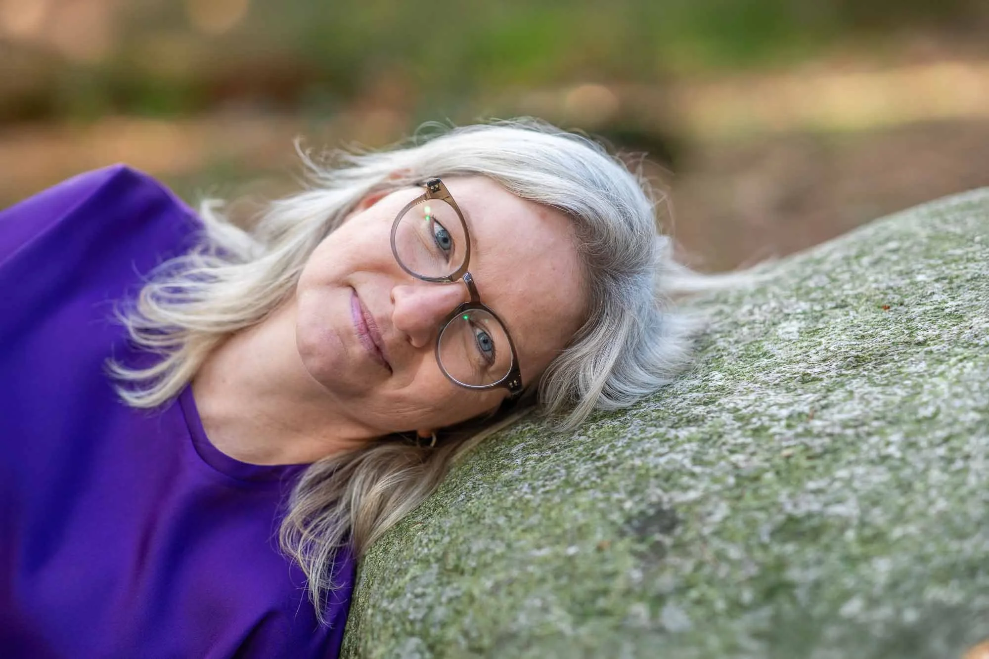 Marieke Buijsse in de natuur met haar hoofd rustend op een steen tijdens een moment van verstilling en reflectie rondom verlies en rouw.