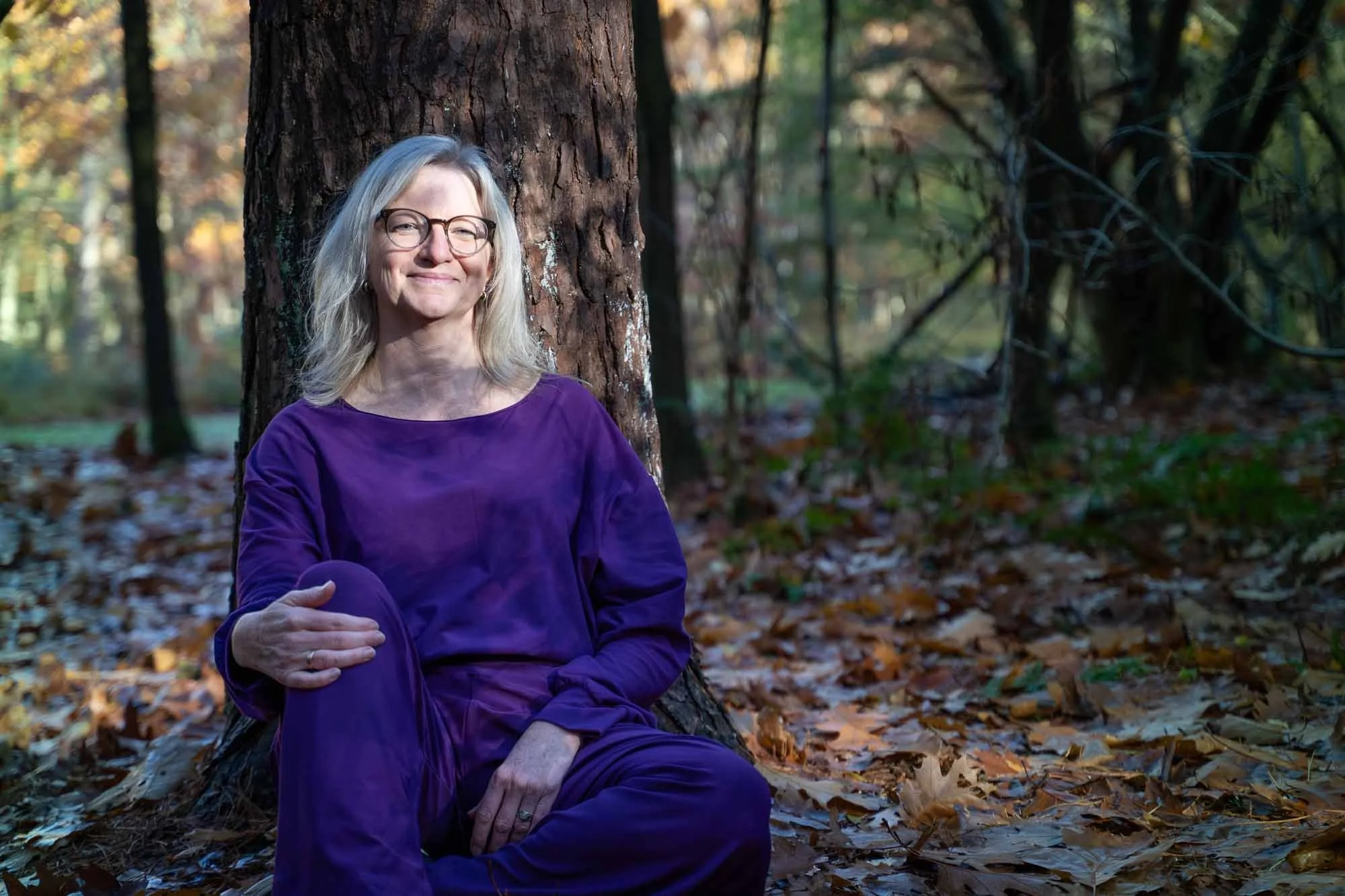 Marieke natuurcoach zit tegen boom in het bos met zonlicht op gezicht