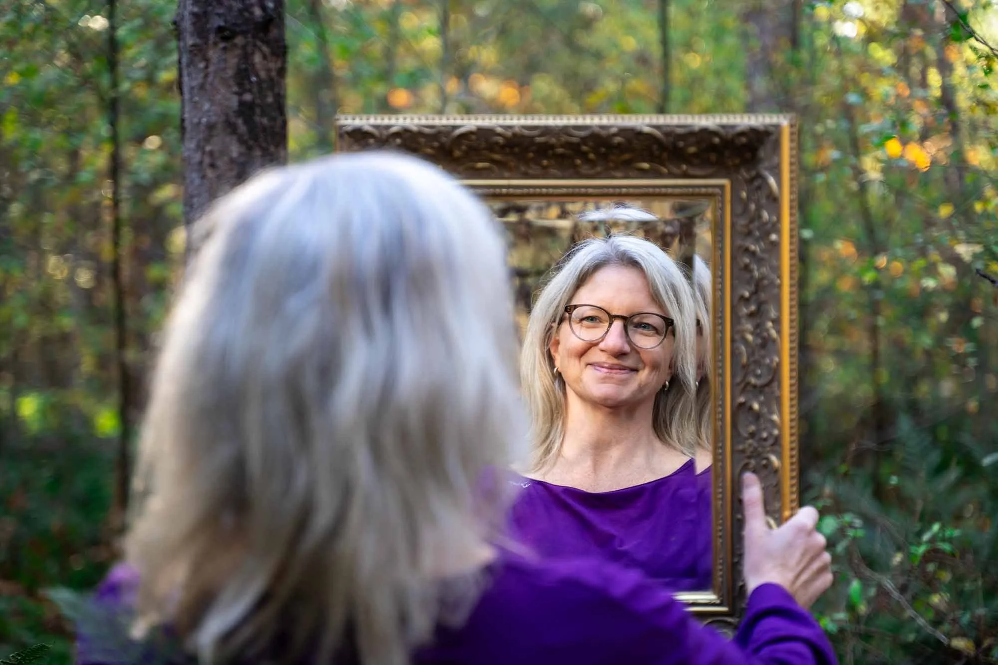 Marieke natuurcoach lacht naar zichzelf in een spiegel in de natuur