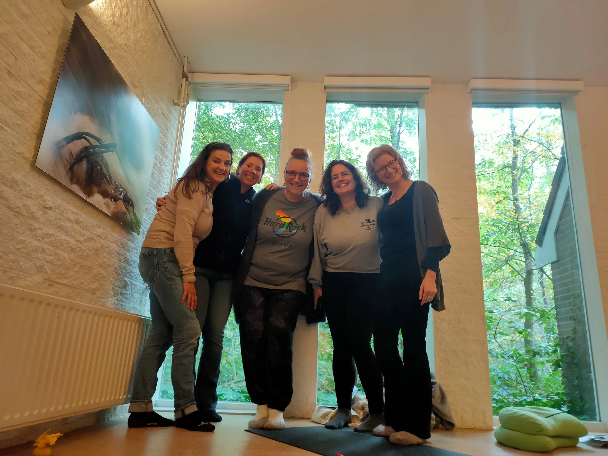 Vijf vrouwen die samen in het Boshuis staan, lachend en poseren voor de camera. Achter hen grote ramen met het groen Mastbos zichtbaar buiten.