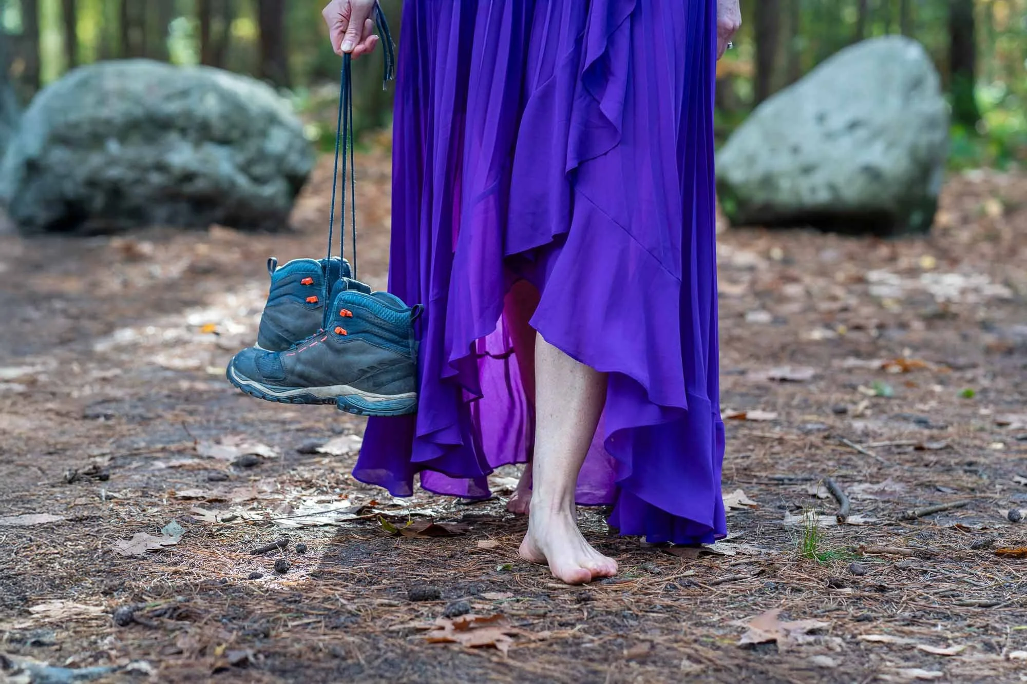 Marieke loopt met blote voeten over de bosgrond en draagt haar wandelschoenen in de hand