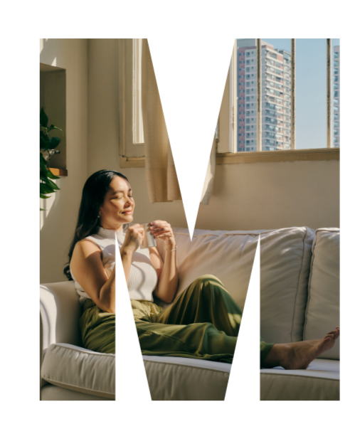 Woman relaxing on a white sofa in a sunlit apartment with city buildings visible through the windows