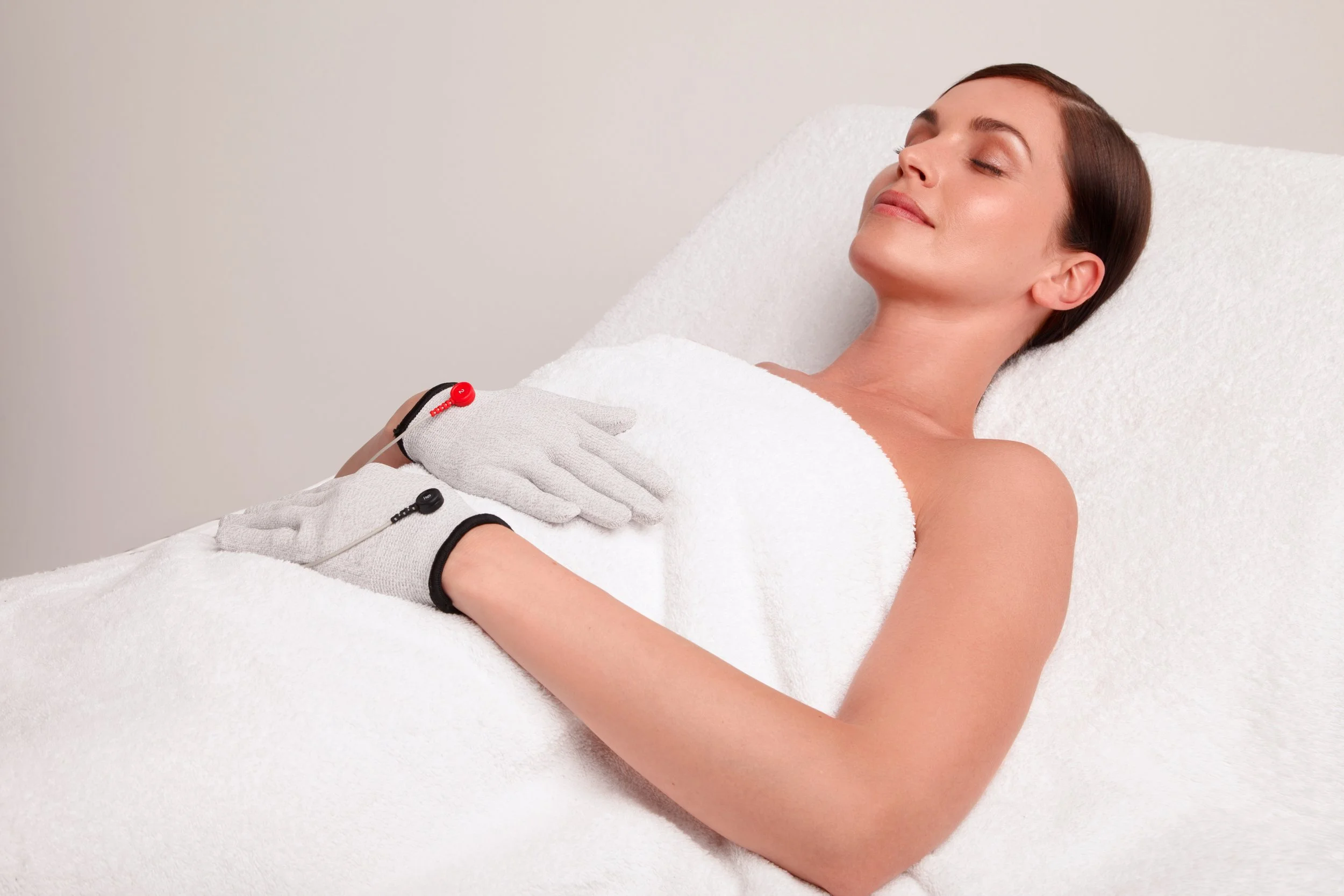 A woman lying on a white padded surface, receiving a seamless cold therapy treatment with her eyes closed and a relaxed expression.