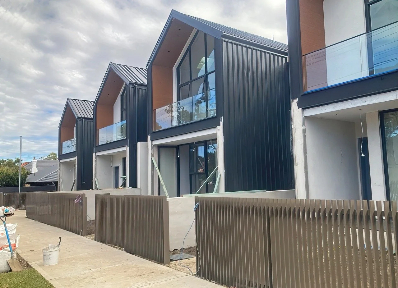 Under construction modern townhouses with black metal siding and large glass balconies.