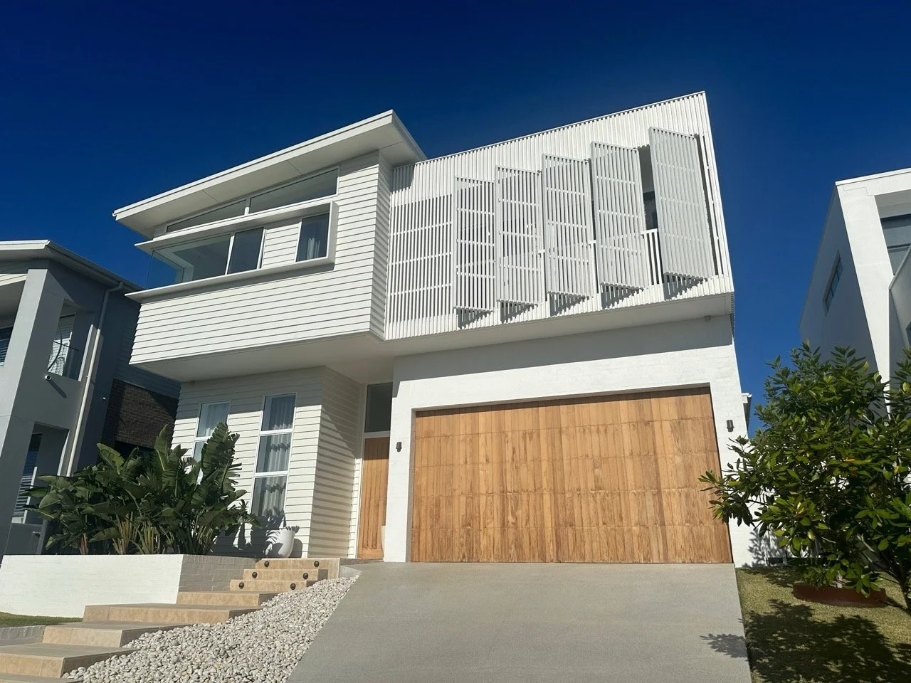 Modern white house with wooden garage door, plants, and a clear blue sky