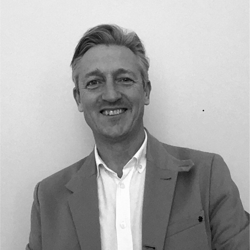 Black and white photo of a smiling man in a suit with a white shirt against a plain background.