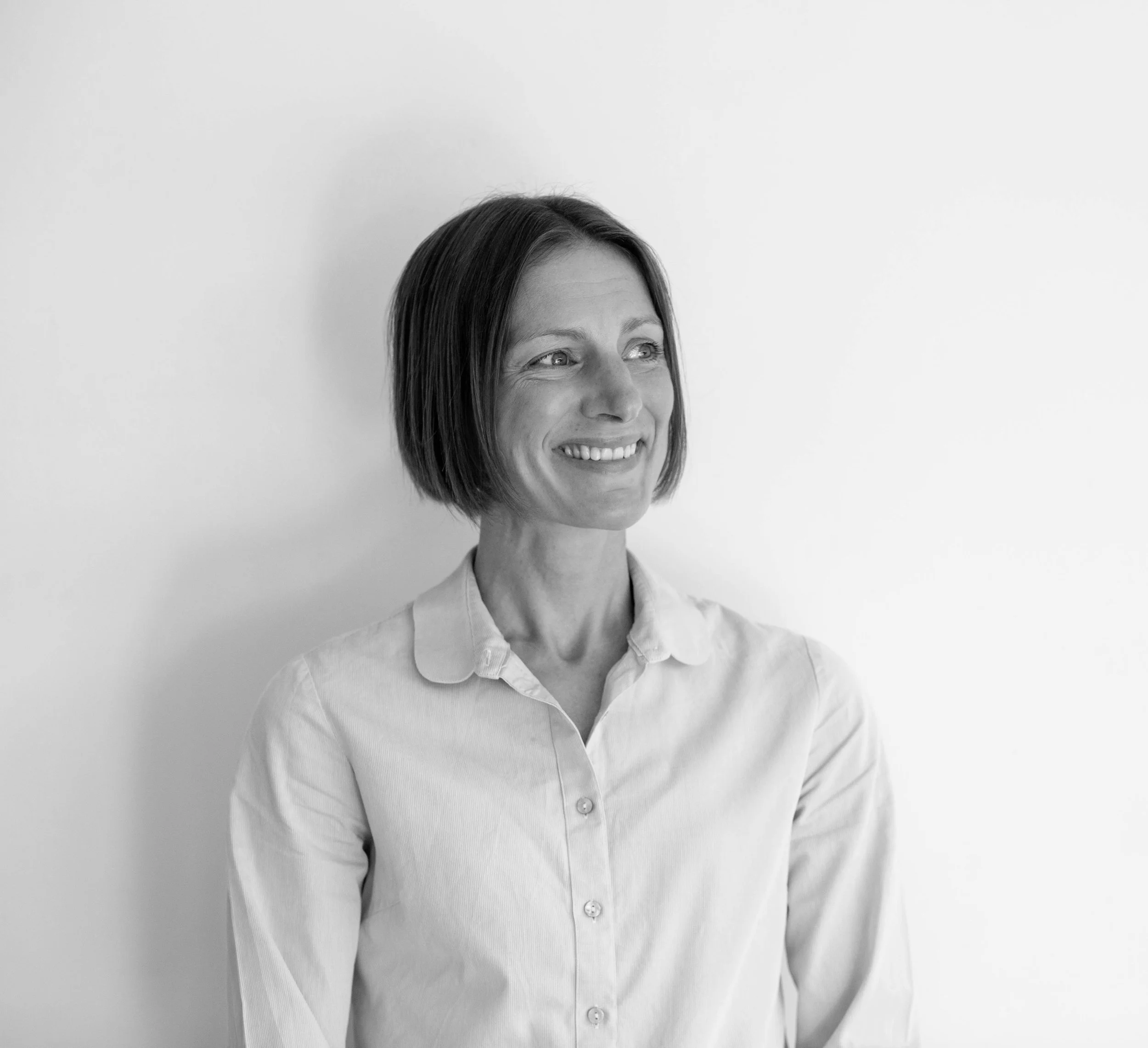 Black and white portrait of a smiling woman with shoulder-length hair, wearing a collared shirt, standing against a plain background.