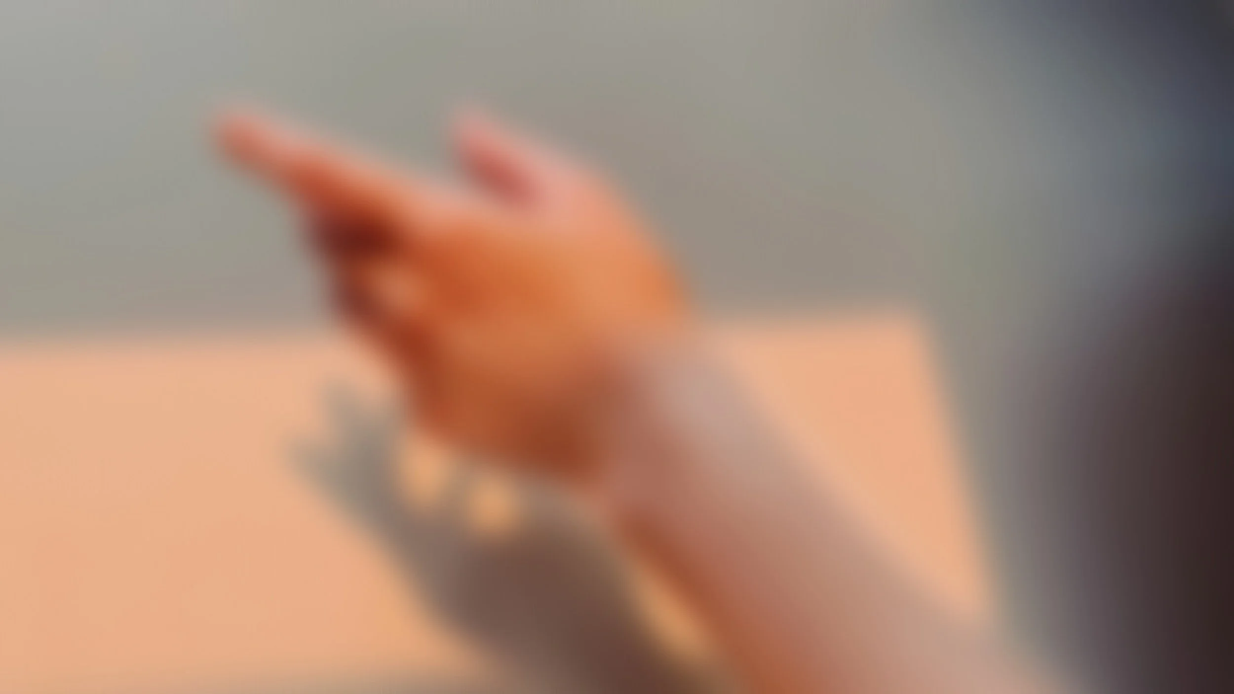 An out-of-focus image showing a hand with fingers extended, set against a blurred background.