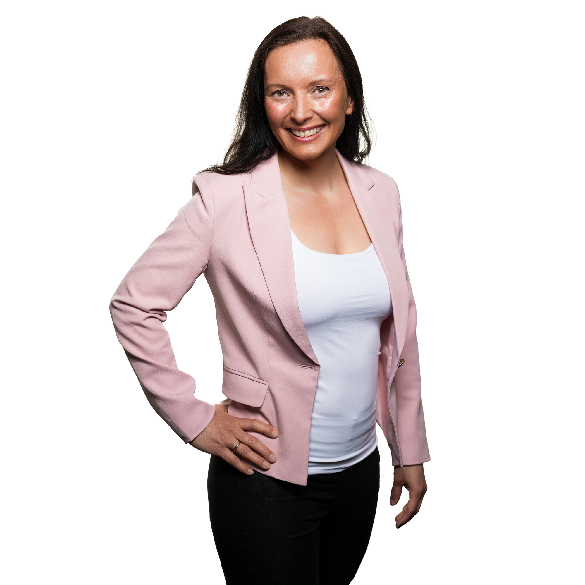 Smiling woman wearing a light pink blazer and black pants, standing with one hand on her hip against a neutral background.