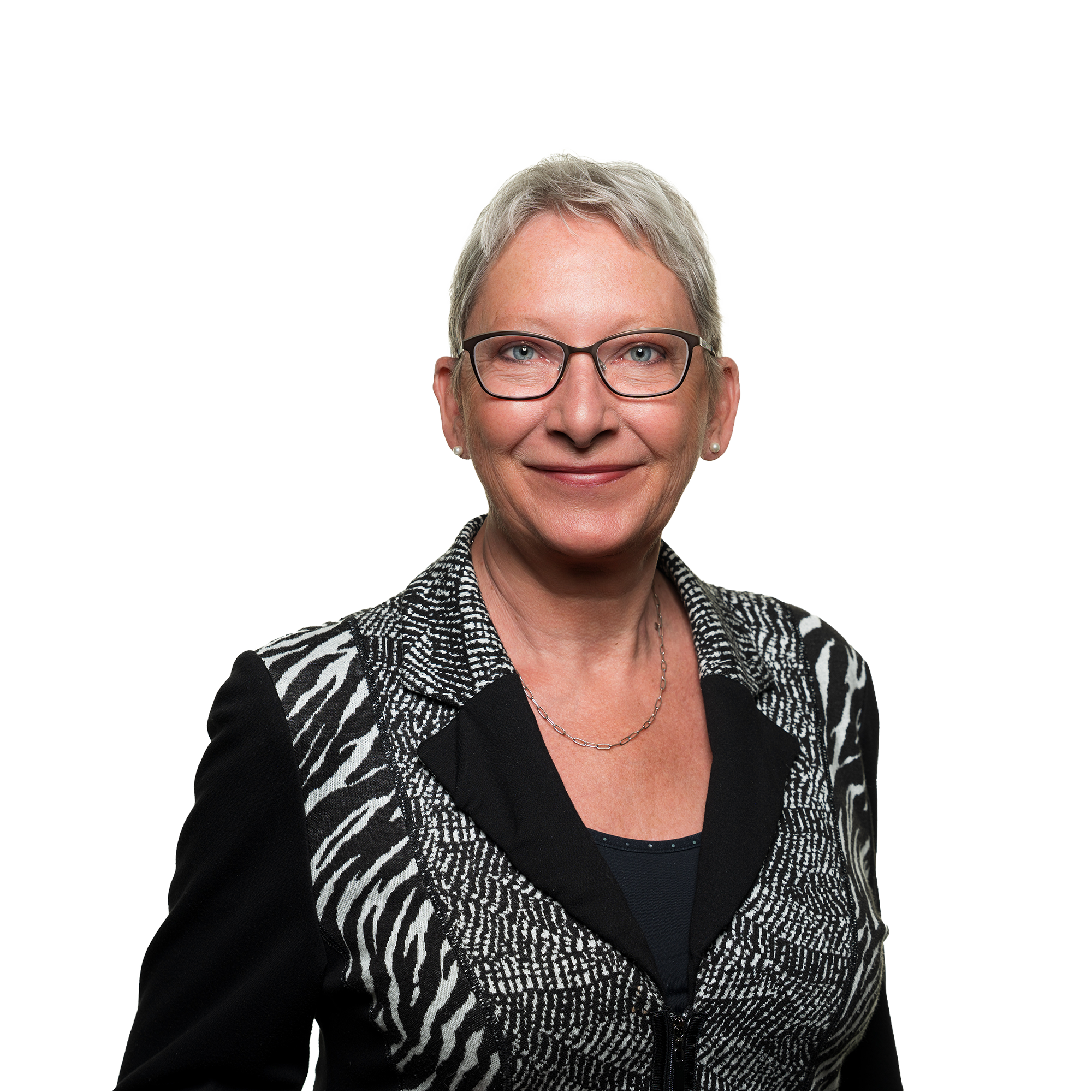 Close-up of a smiling middle-aged woman with short gray hair, wearing glasses, a black top, and a black and white patterned blazer, against a plain background.