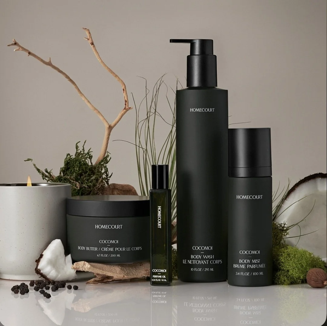 Homecourt Cocomoi body care collection styled with natural elements, including moss, coconut, and branches, against a neutral background.