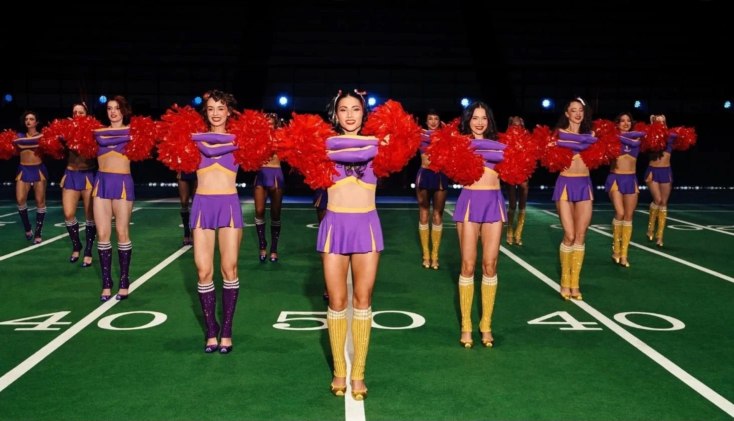 Cheerleaders perform on a football-inspired runway at Christian Louboutin’s Paris Fashion Week show, wearing purple uniforms, red pom-poms, and gold heels with the brand’s signature red soles.