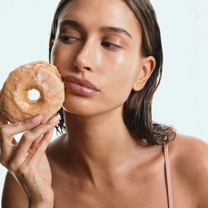 A woman with wet hair holding a glazed donut near her face