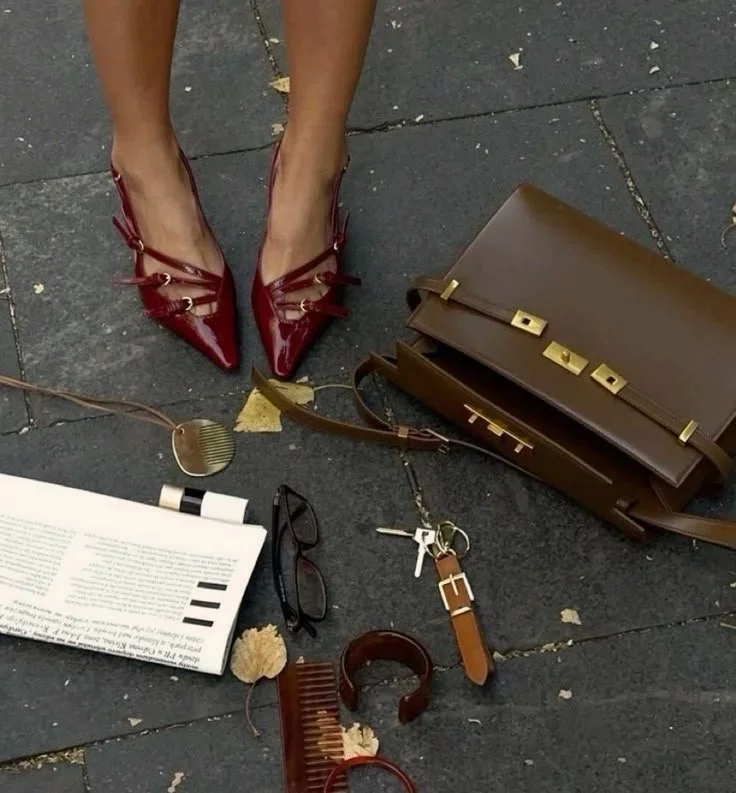 Editorial flat lay featuring a brown structured handbag, red heels, and lifestyle essentials — representing urban sophistication and brand storytelling