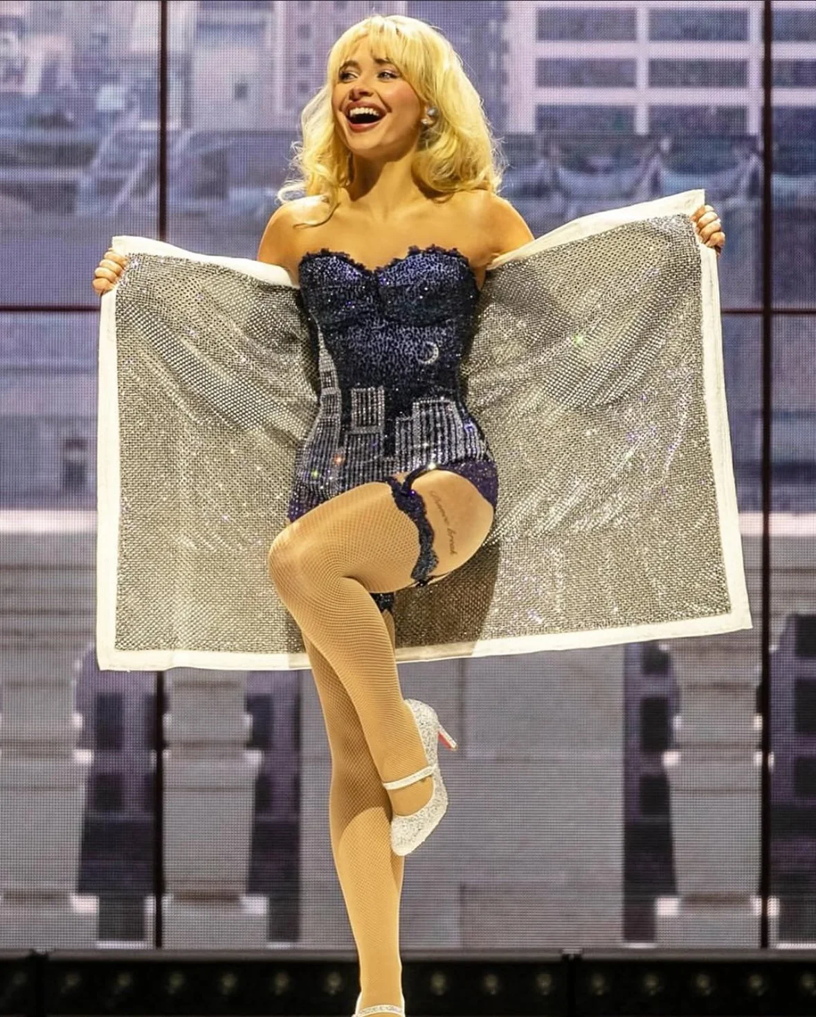 Sabrina Carpenter performing in sparkling corset dress and Louboutin heels on stage, dramatic reveal moment during stadium tour show.