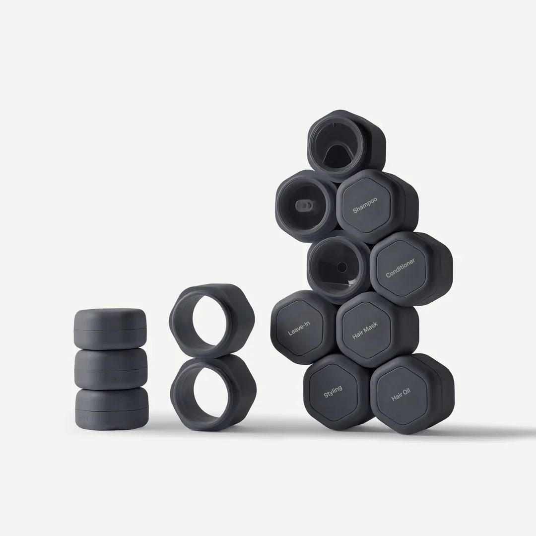 Sleek modular Cadence travel containers in dark matte tones stacked in geometric formation, showcasing minimalist refillable packaging for personal care products.
