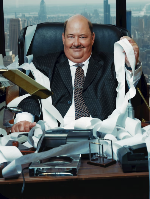 Man in a suit sitting at an office desk surrounded by financial papers and receipts, styled humorously to illustrate chaotic bookkeeping. Corporate parody tone often used in viral marketing and finance-tech promotions.