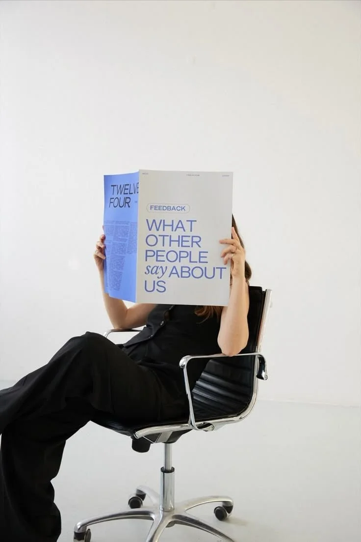Person seated on a modern chair reading a bold blue poster titled “What Other People Say About Us.”