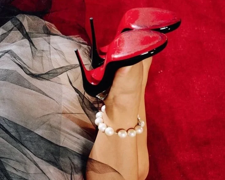 Close-up of iconic Christian Louboutin red-soled heels resting on a red carpet, symbolizing the brand’s signature blend of luxury and sensuality.