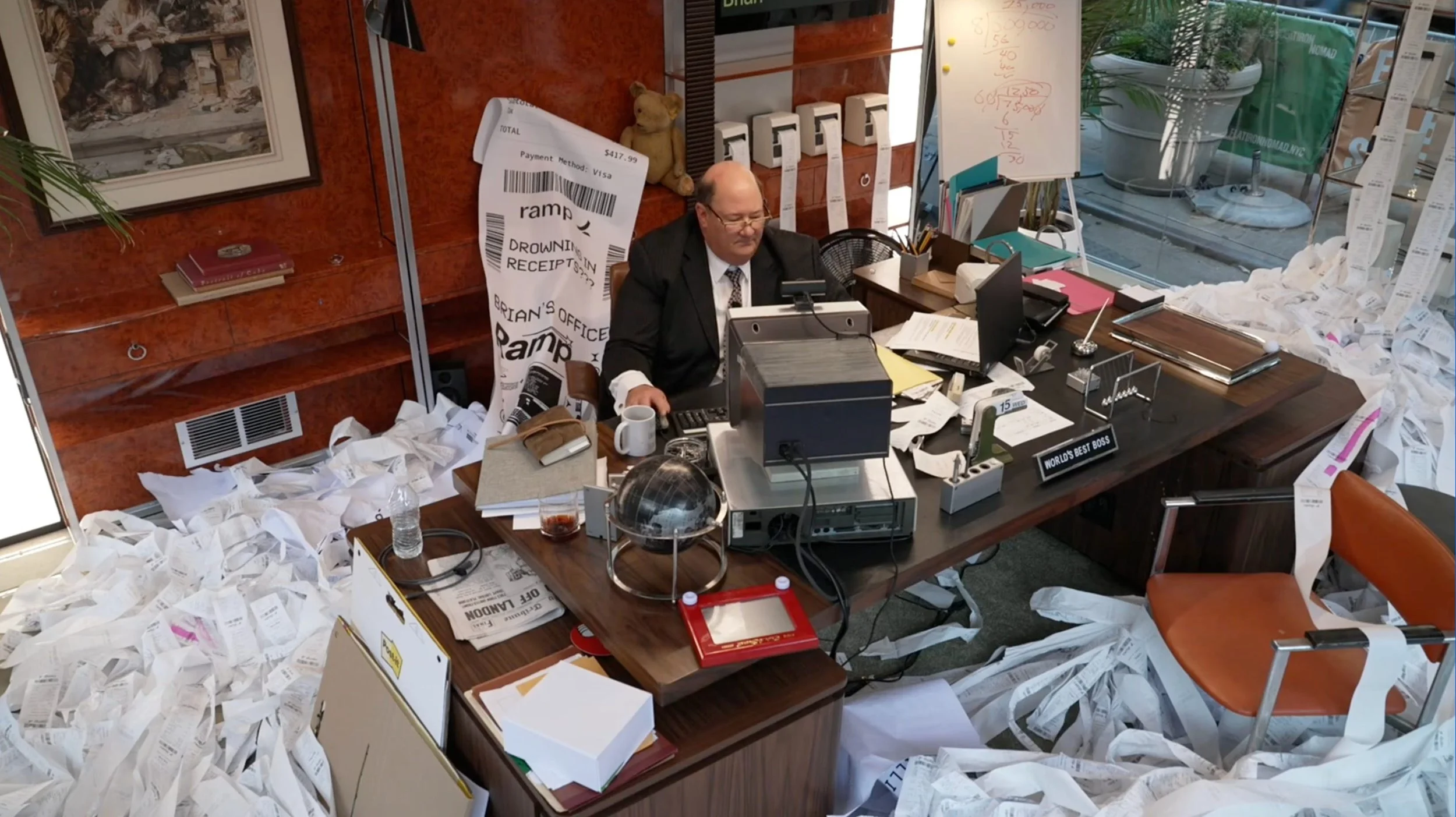 Brian Baumgartner as Kevin Malone inside Ramp’s glass box office activation in New York City, surrounded by overflowing receipts while manually processing expenses during the live fintech marketing stunt.