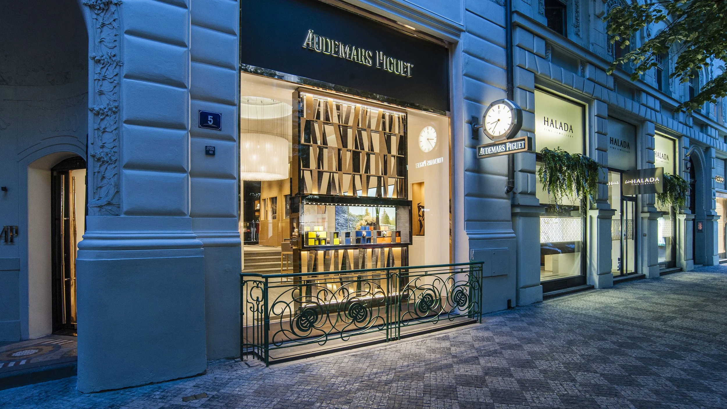 The storefront of Audemars Piguet, a luxury watch retailer, with illuminated signage and clocks on the facade, located on a city street at night.