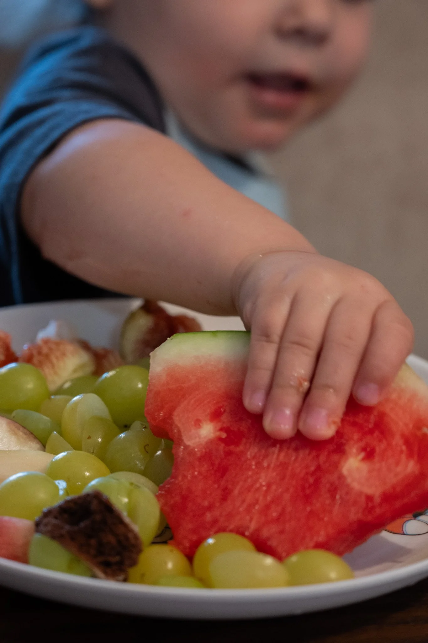 יד של ילדה מושיטה יד לפרוסת אבטיח מצלחת פירות