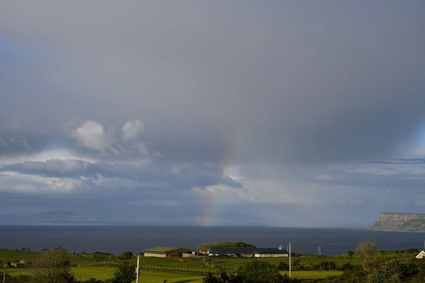 קשת בענן מעל ים כחול וכפר קטן על מצוק ירוק – צפון אירלנד