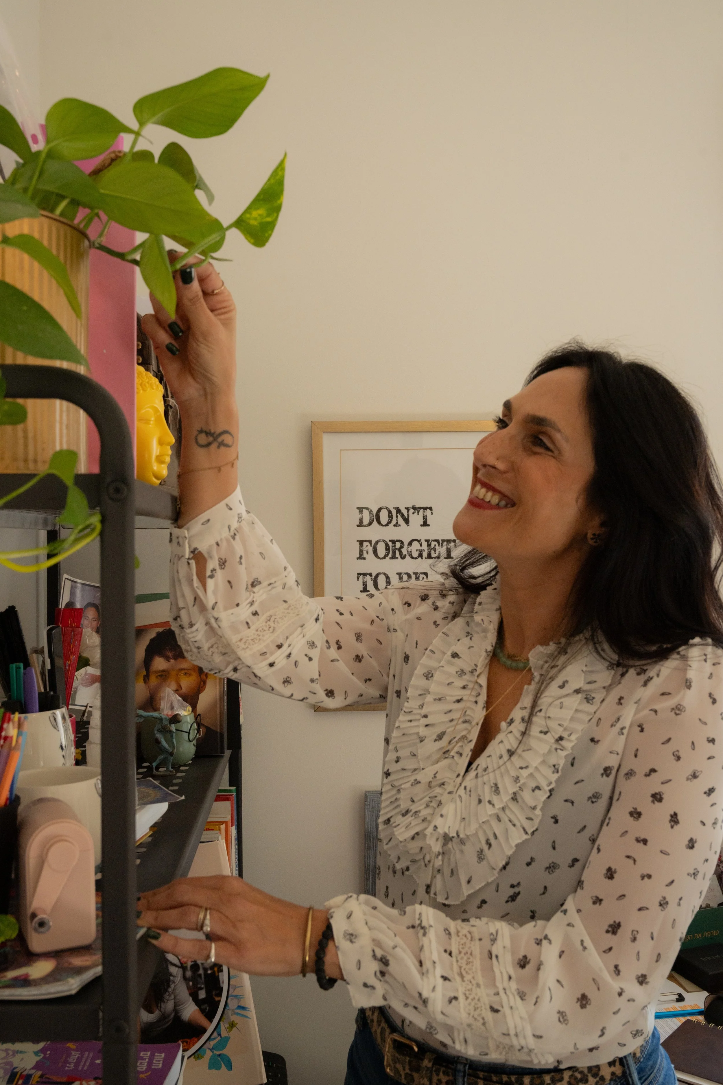 Limor smiles as she reaches up to tend a green plant