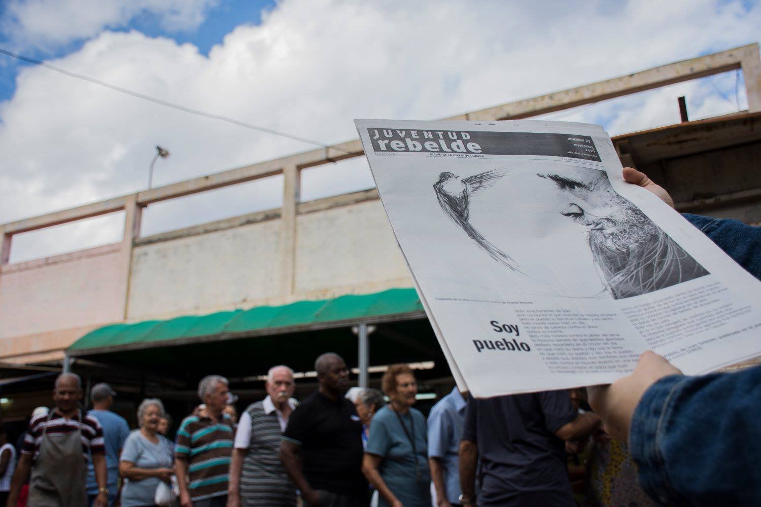 המון אנשים ברחוב בעוד גבר מקריא שער עיתון המוקדש לפידל קסטרו