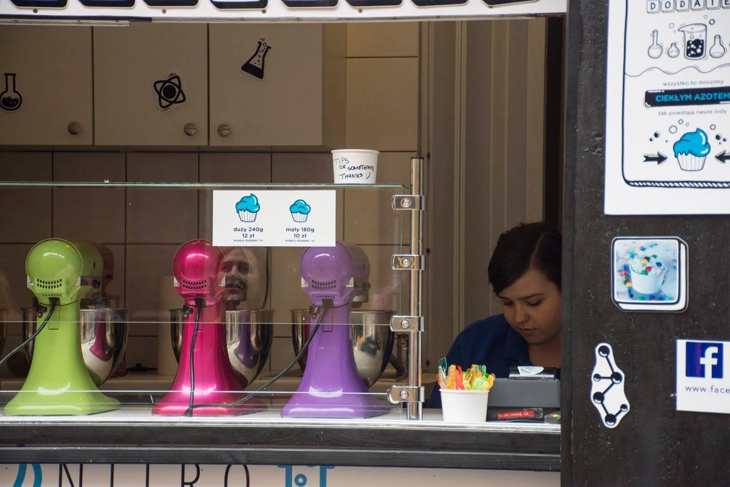 חלון חנות קינוחים עם מכונות עירבול צבעוניות בזמן שעובדת מכינה הזמנות מאחורי הדלפק